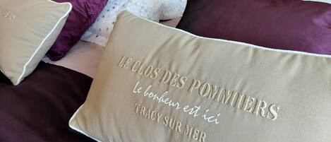 Uma cama com vários travesseiros, incluindo um bordado com texto em francês.
