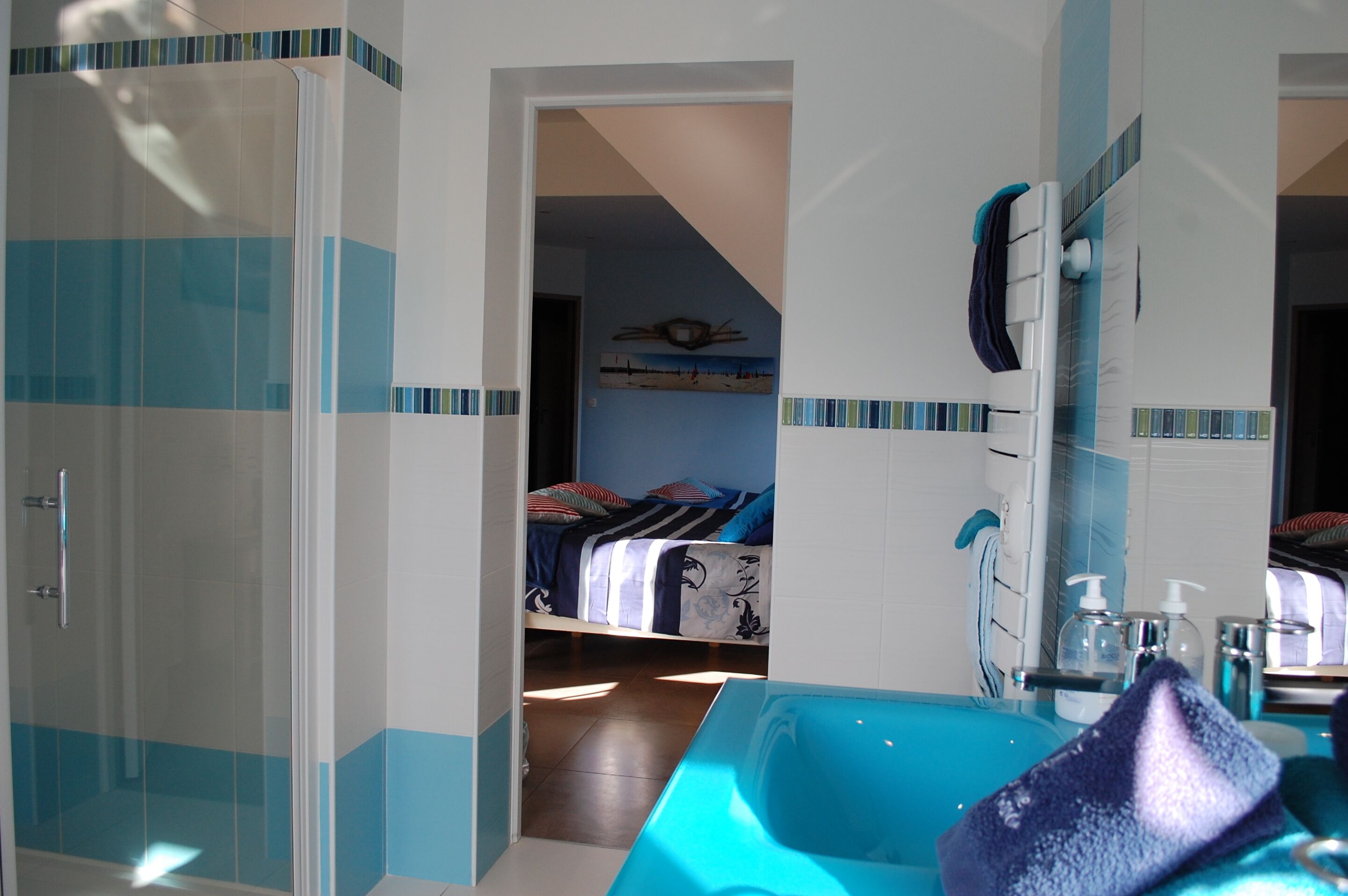 A bathroom with a glass shower enclosure, a large bathtub, and a bed in the adjacent room.