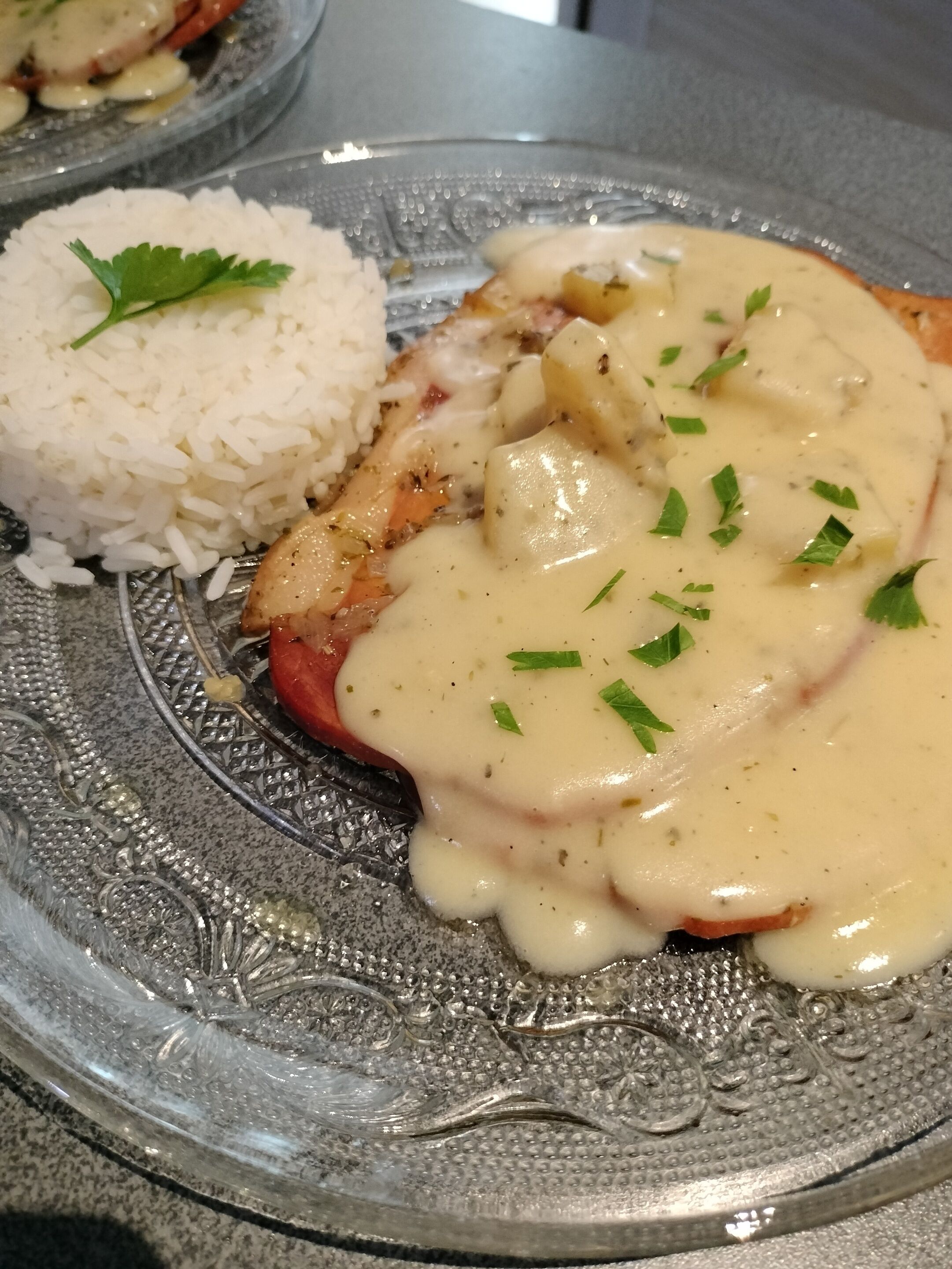 A plate with a piece of meat covered in sauce, accompanied by a side of white rice, all served on an intricately designed glass plate.