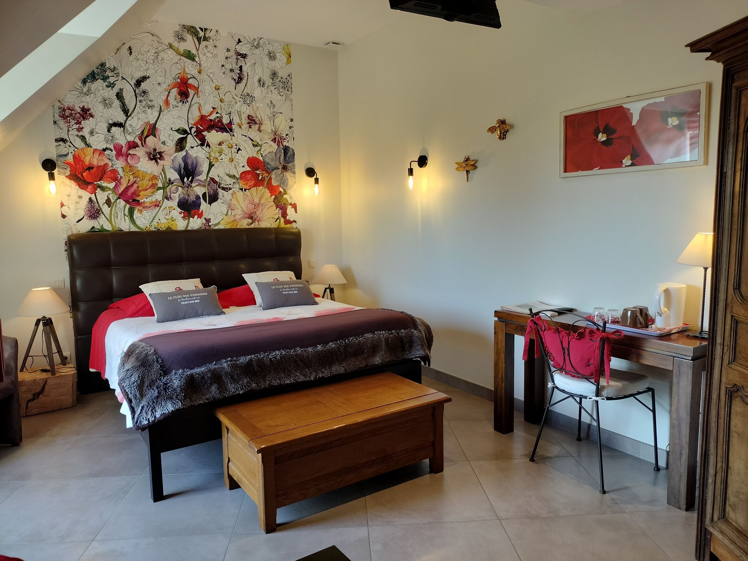 Un dormitorio con una cama grande, un banco de madera, un escritorio con una silla y una pared decorada con motivos florales.
