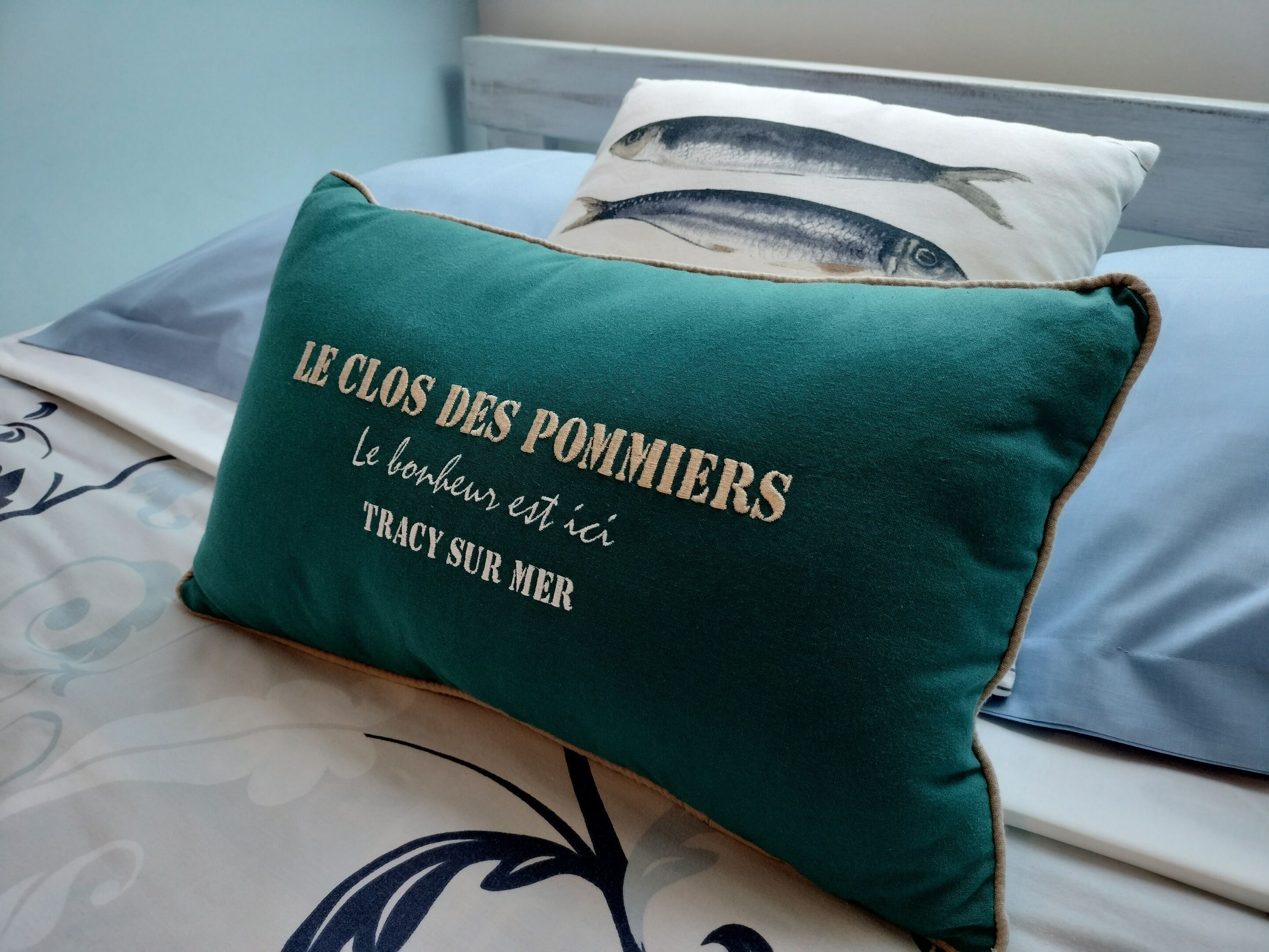 Un almohárraga color turquesa con texto en francés sobre una cama con ropa de cama estampada.