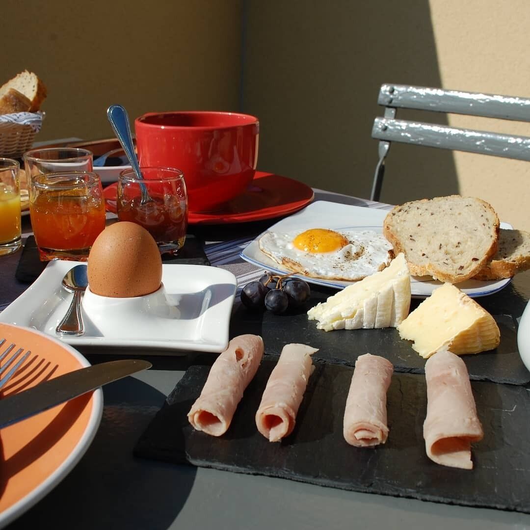 Una mesa de desayuno con huevos, pan, queso, jamón y una taza roja.