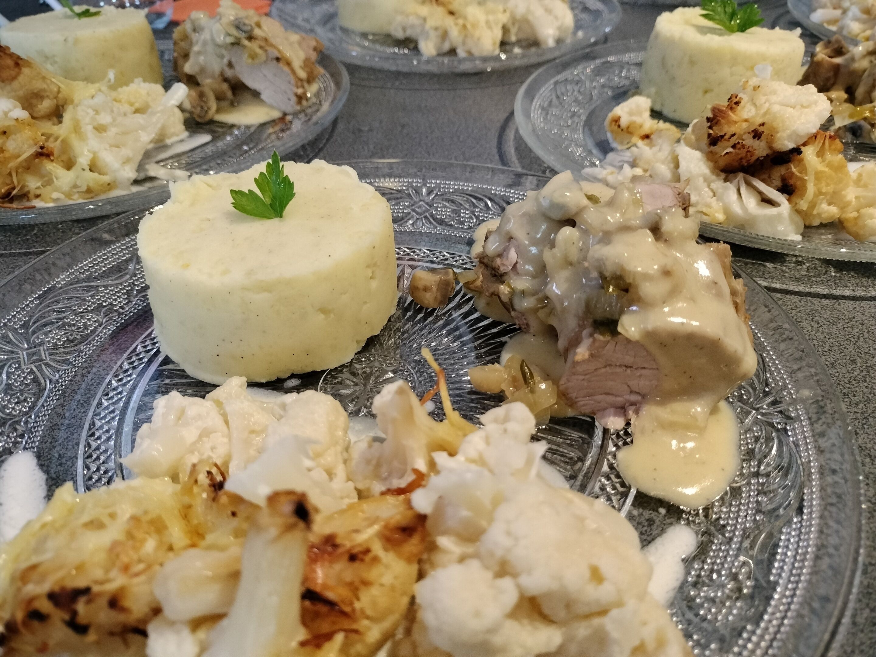 Une table à manger avec différents plats, notamment de la purée de pommes de terre, de la viande et du chou-fleur.