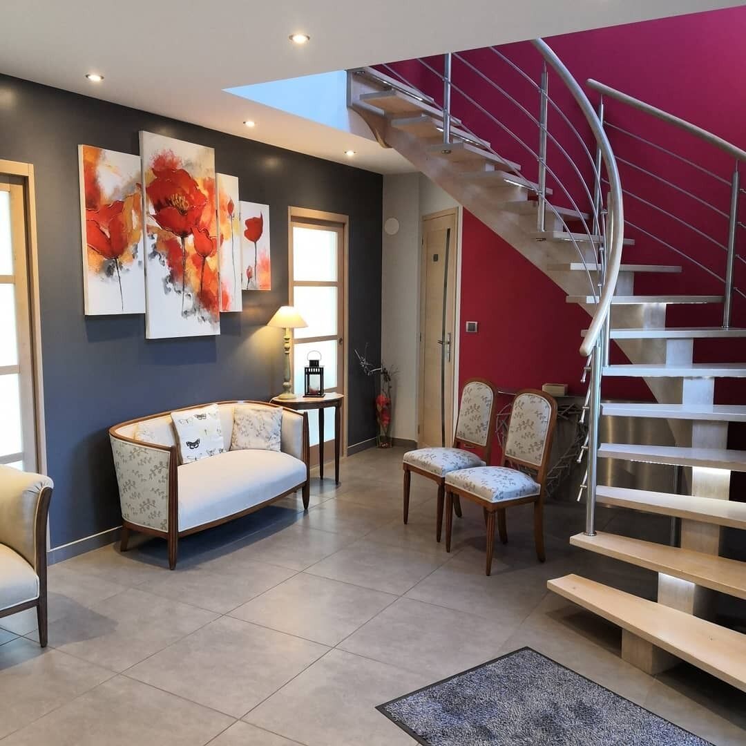 Una sala de estar moderna con un sofá, sillas, una mesita de centro y una escalera con una pared de acento roja.
