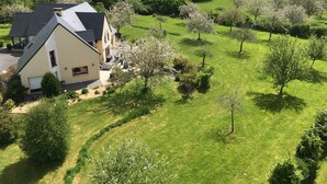 A two-story house with a sloped roof, surrounded by a well-maintained lawn and flowering trees. - Le Clos des pommiers (Tracy-sur-Mer)