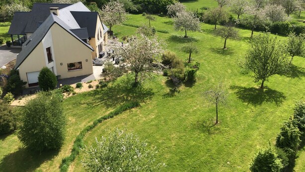 A two-story house with a sloped roof, surrounded by a well-maintained lawn and flowering trees. - Le Clos des pommiers (Tracy-sur-Mer)