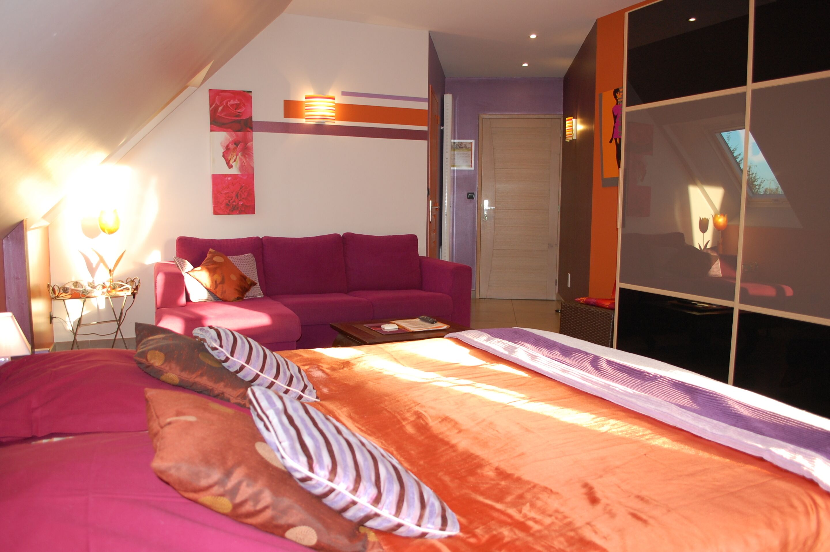 A bedroom with a bed, a pink sofa, a small table, and a large window.