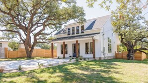A modern two-story house with a large tree in the front yard. - WineHaus with Pool and Hot Tub (Fredericksburg)