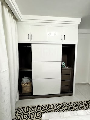 A white wardrobe with multiple drawers and a hanging section, a laundry bag, and a patterned rug. - Modern 1BR in Westlands near GTC, Sarit, JW Marriott & Villa Rosa Kempinski (Nairobi)