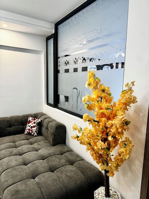 A modern living room with a grey sofa, a decorative wall piece, and a vase of yellow flowers. - Modern 1BR in Westlands near GTC, Sarit, JW Marriott & Villa Rosa Kempinski (Nairobi)