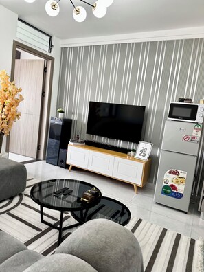 Ein modernes Wohnzimmer mit Flachbildfernseher, einem weißen Schrank, einem Glastisch und einer gestreiften Wand.