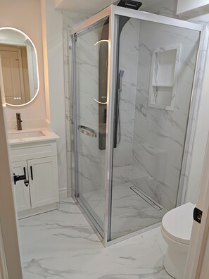 A modern bathroom with a glass-enclosed shower, a white sink with a mirror, and a toilet. - Newly renovated stylish 3B3B basement suite with full kitchen (Richmond Hill)