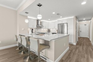 A modern kitchen with a large island, bar stools, stainless steel appliances, and pendant lighting. - Palazzo 1206 (Panama City Beach)