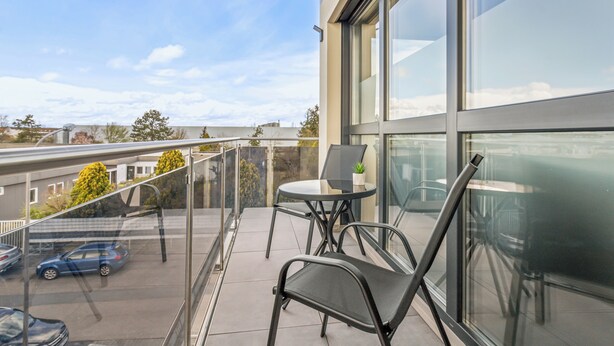 Ein Balkon mit Glasgeländer, einem Tisch, zwei Stühlen und einem Blumentopf.