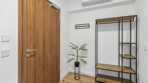 Ein Zimmer mit Holztür, einem schwarzen Metallregal, einem Topfpflanzen und einer Wand-Klimaanlage.