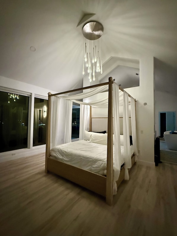 Une chambre moderne avec un lit à baldaquin, de grandes fenêtres et un luminaire au plafond.