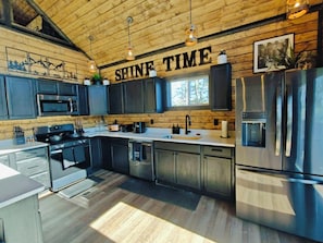 A modern kitchen with wooden ceiling, stainless steel appliances, and a 'SHINE TIME' sign. - Shine Time Smoky Mtn Cabin Views 2BR (Sevierville)