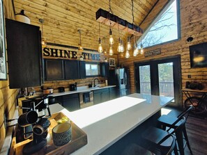 A modern kitchen with a large island, wooden walls, and pendant lighting. - Shine Time Smoky Mtn Cabin Views 2BR (Sevierville)