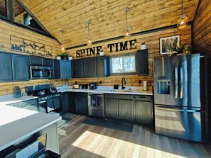 A modern kitchen with wooden walls, stainless steel appliances, and a 'SHINE TIME' sign. - Shine Time Smoky Mtn Cabin Views 2BR (Sevierville)