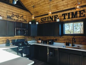 A modern kitchen with wooden cabinetry, stainless steel appliances, and a large window. - Shine Time Smoky Mtn Cabin Views 2BR (Sevierville)