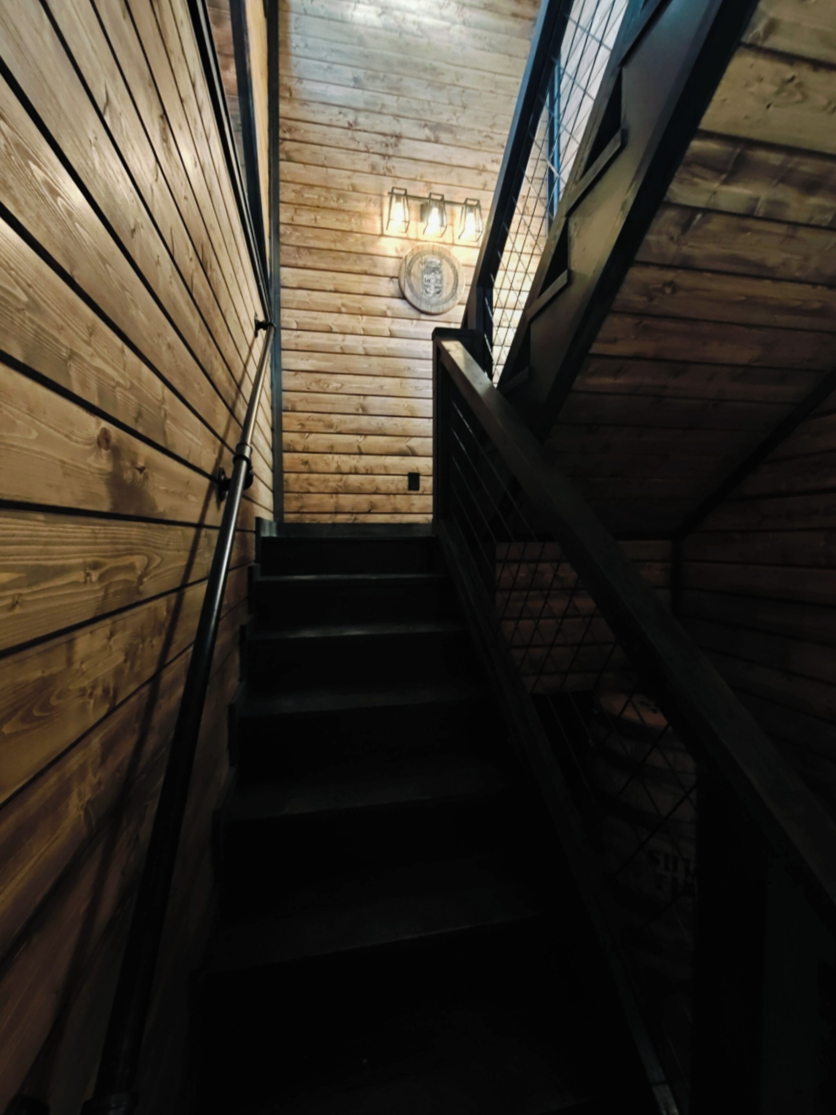 A wooden staircase with a metal handrail and a wall-mounted light fixture.