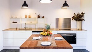 Una cocina moderna con armarios blancos, una isla de madera y dos lámparas colgantes.