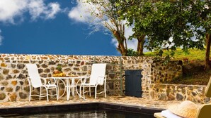 Un espacio al aire libre con paredes de piedra, piscina, sillas blancas y una mesa.