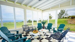 Un patio cubierto con piso a cuadros, sillas Adirondack verdes y una mesa con fruta.