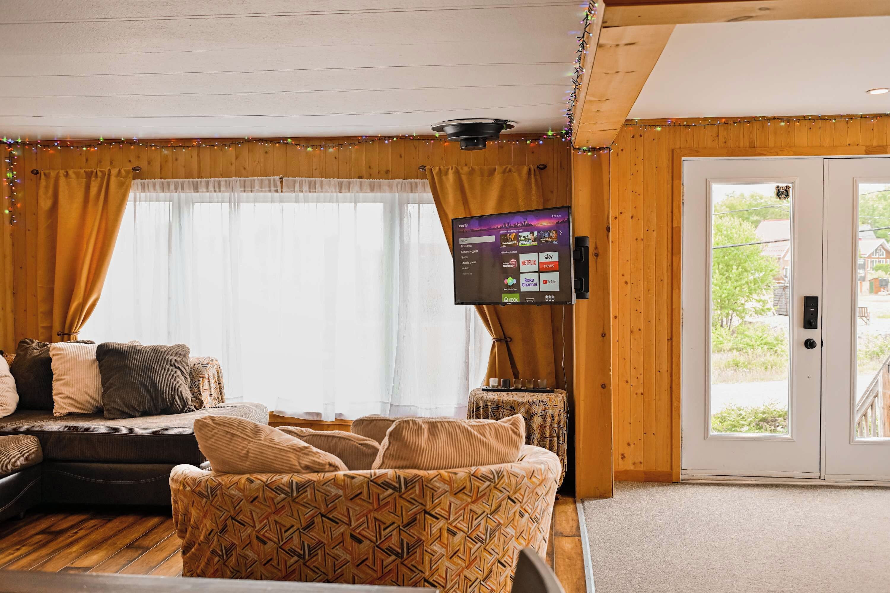 A cozy living room with a sofa, patterned cushions, a flat-screen TV mounted on the wall, and a wooden door leading outside.