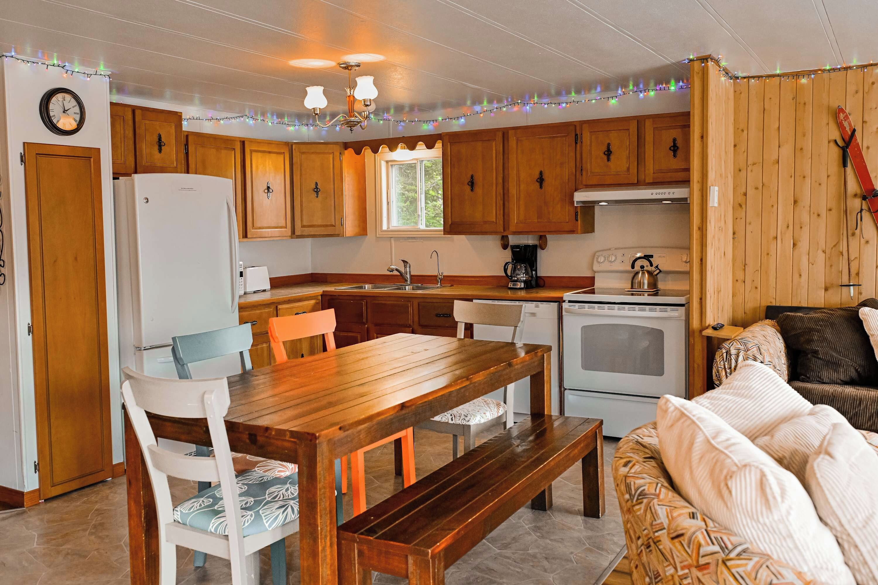 A compact kitchen with wooden cabinets, a refrigerator, a stove, and a dining area with a table and chairs.