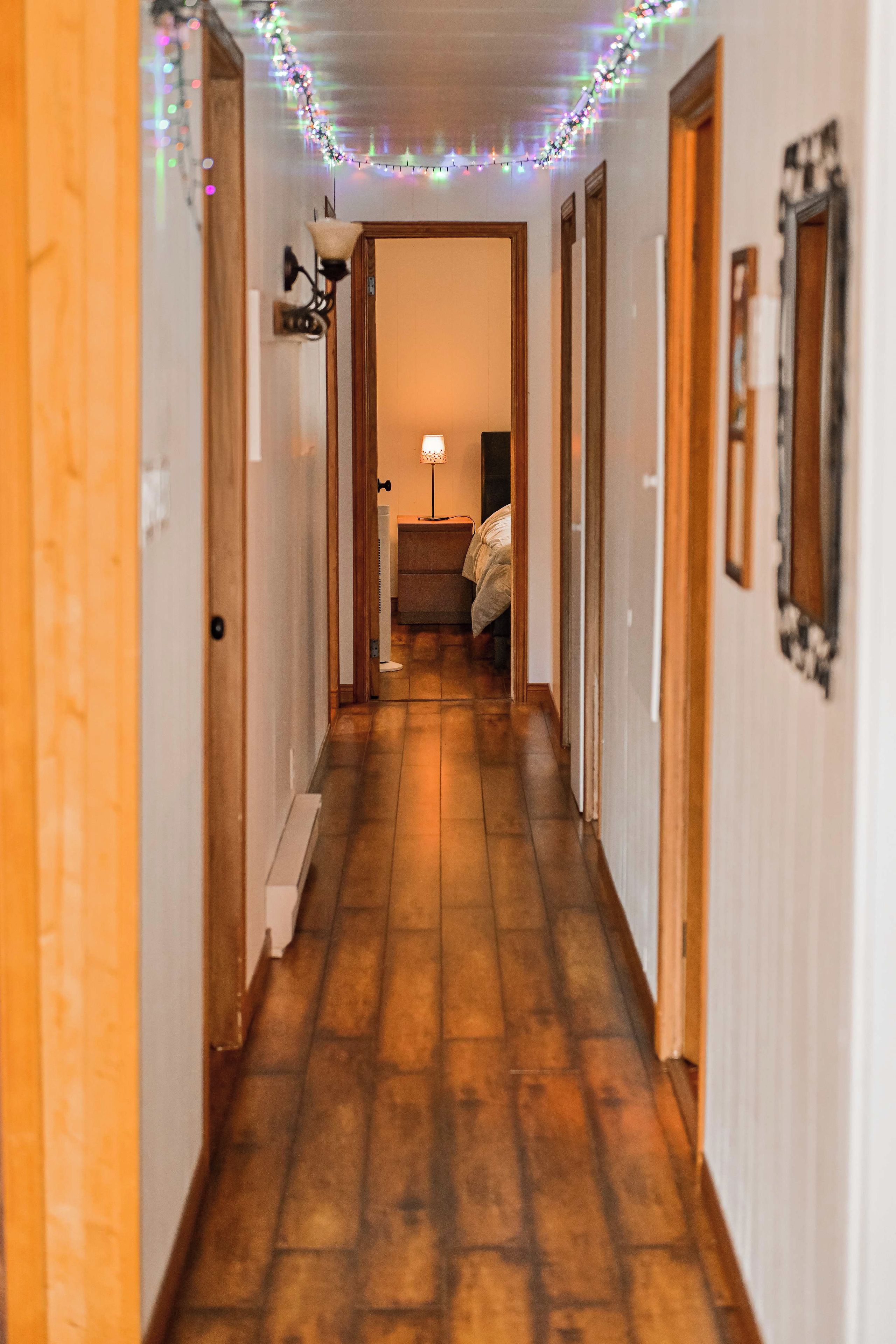 Um corredor com piso de madeira, uma cama e uma luminária ao fundo.
