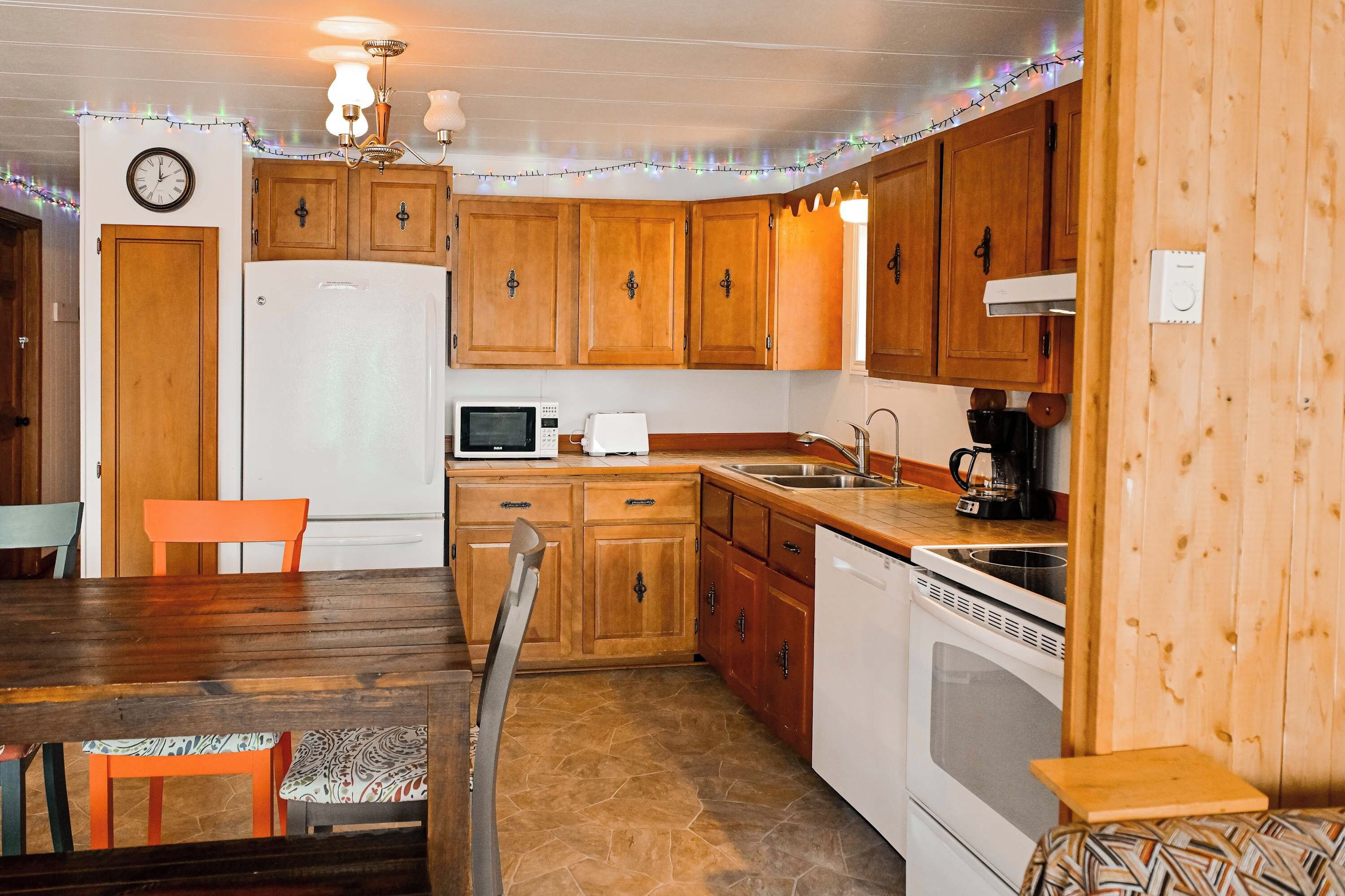 A compact kitchen with wooden cabinets, a refrigerator, microwave, stove, and a dining area with a table and chairs.