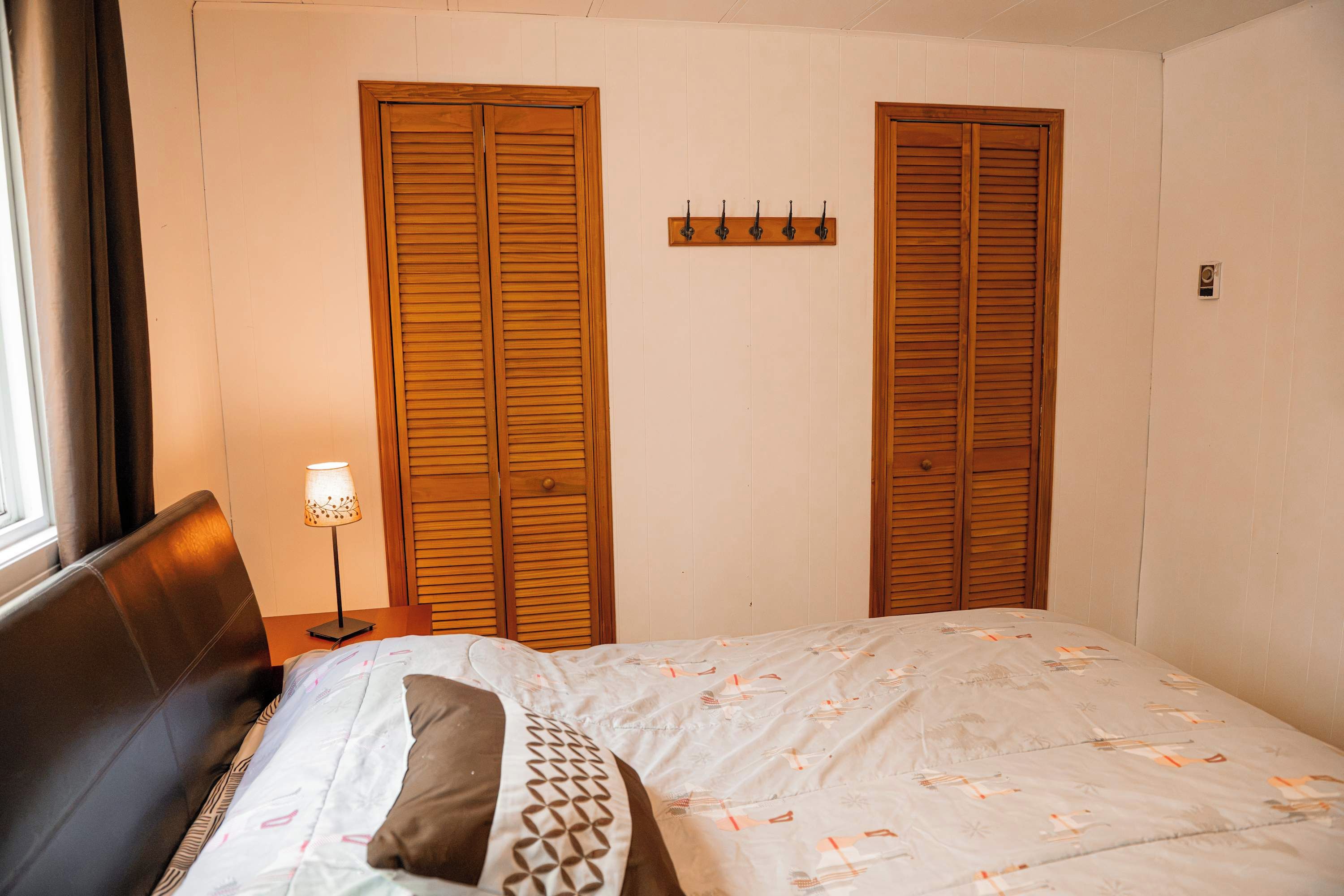 A bedroom with a bed, a nightstand, a lamp, and two wooden wardrobes.
