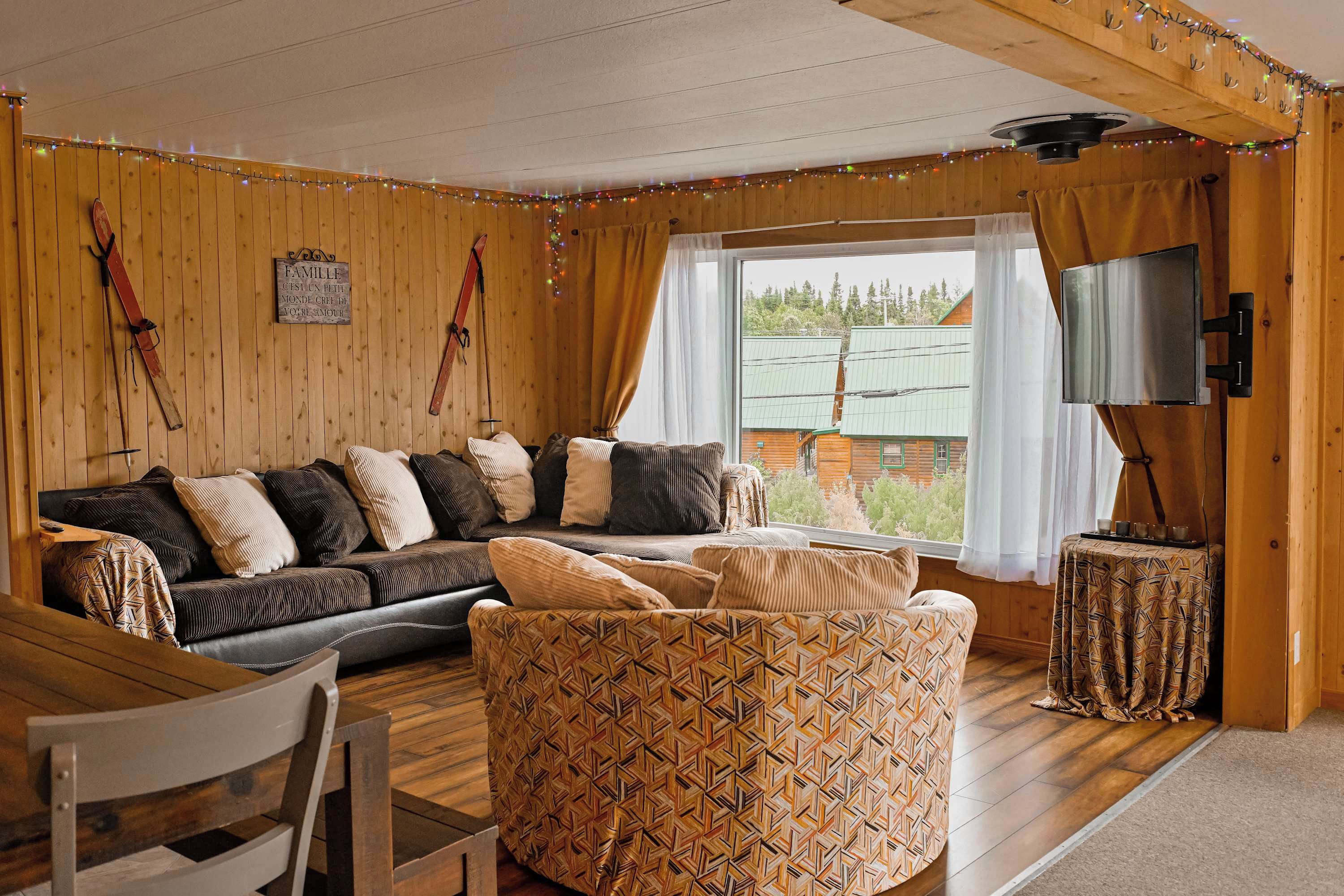 Interior acolhedor de uma cabana com um sofá, um banquinho estampado e uma área de refeições.
