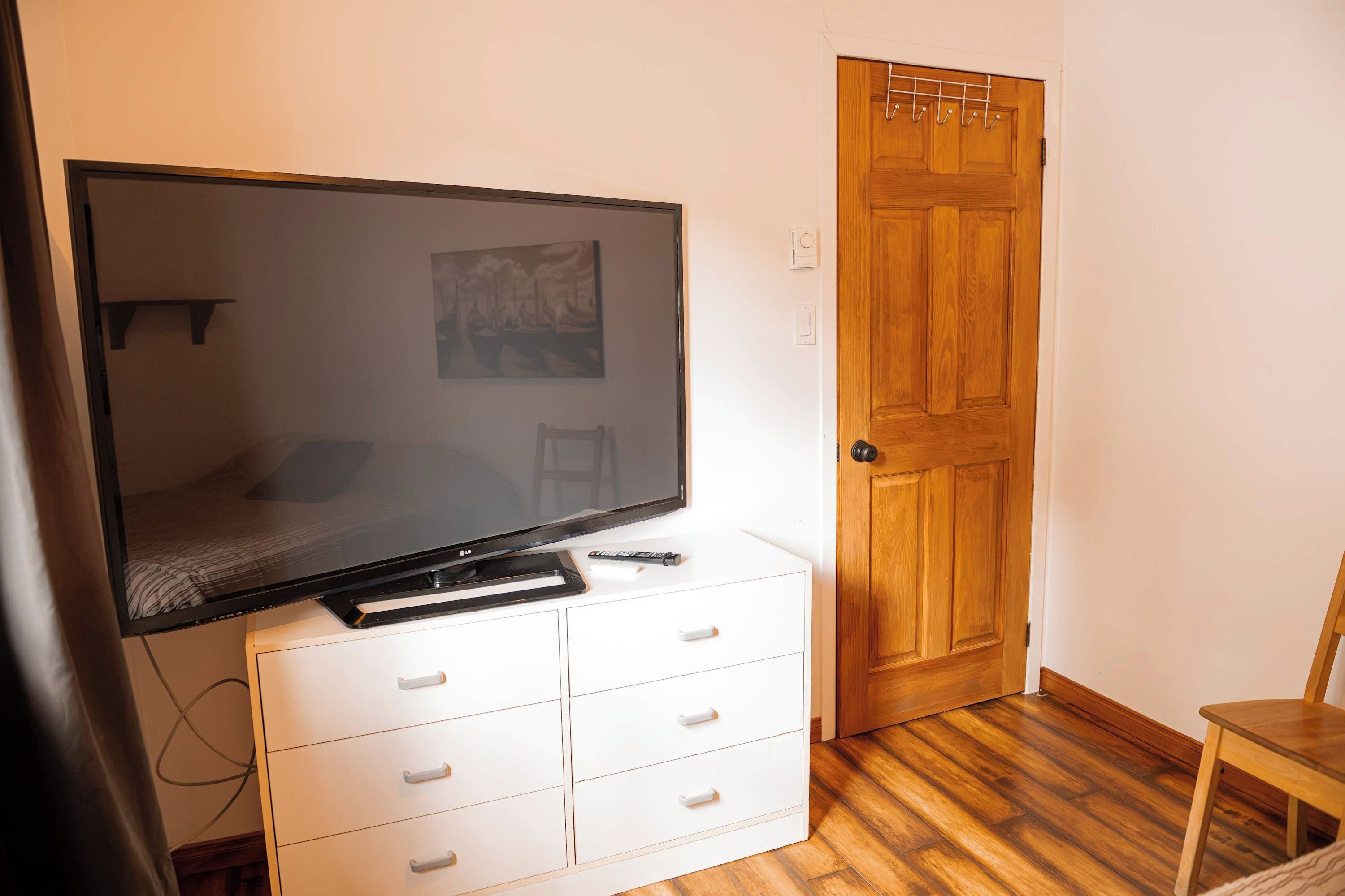 Een kamer met een televisie op een kast, een houten deur en een stoel.