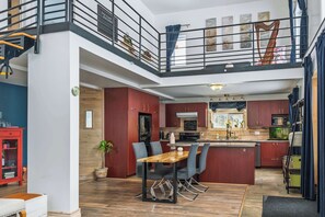 A modern kitchen with a central island, a dining area with a wooden table and chairs, and a staircase leading to an upper level. - L'Ecomaison - Luminous & Open Space (Rouyn-Noranda)