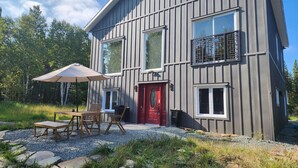 A modern two-story building with a red door, large windows, and a balcony. - L'Ecomaison - Luminous & Open Space (Rouyn-Noranda)