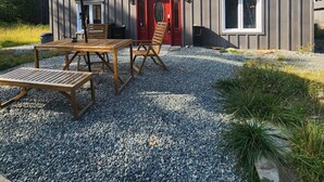 A modern building with a gravel patio, outdoor furniture, and a red door. - L'Ecomaison - Luminous & Open Space (Rouyn-Noranda)
