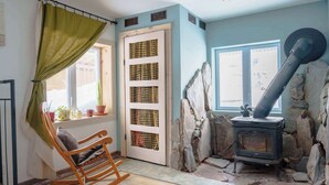 A room with a rocking chair, a stone wall, a wood-burning stove, and a window with a view. - L'Ecomaison - Luminous & Open Space (Rouyn-Noranda)