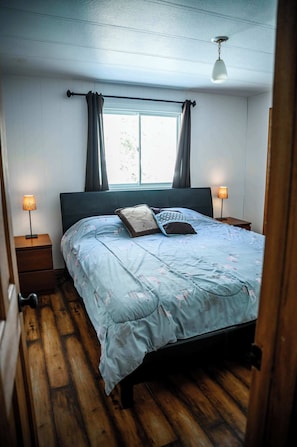 Una camera da letto con un letto, due lampade da comodino, una finestra con tende e un pavimento in legno.