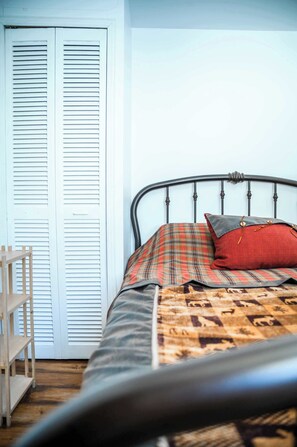 A bed with a metal frame, a plaid blanket, and a red pillow. - Double House - Mont-Video (Barraute)