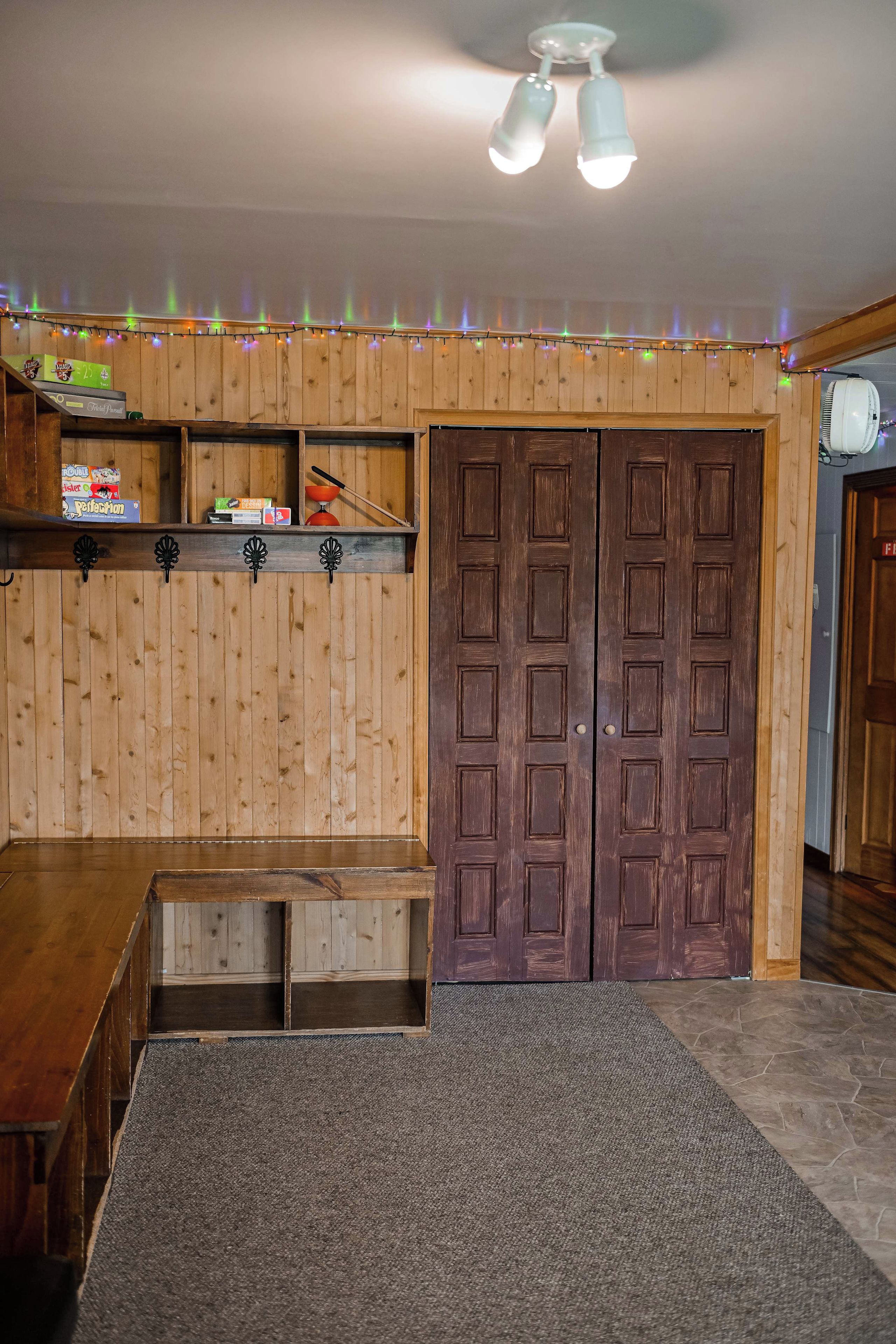 A room with a wooden floor, a bench, a double door, and a ceiling fan.