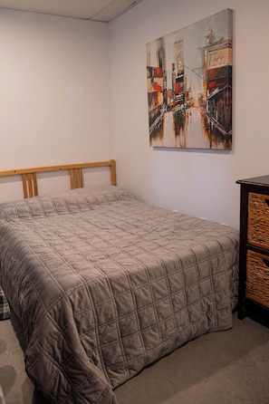 A bedroom with a bed, a headboard, a painting on the wall, and a small wooden cabinet.