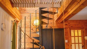 Un interior de madera con una escalera de caracol, una puerta de madera y una pequeña mesa con una silla.
