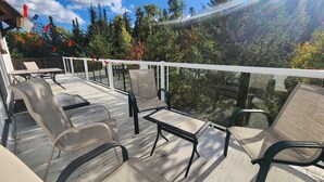Una terraza con mobiliario exterior, barandilla y vista a árboles y cielo.