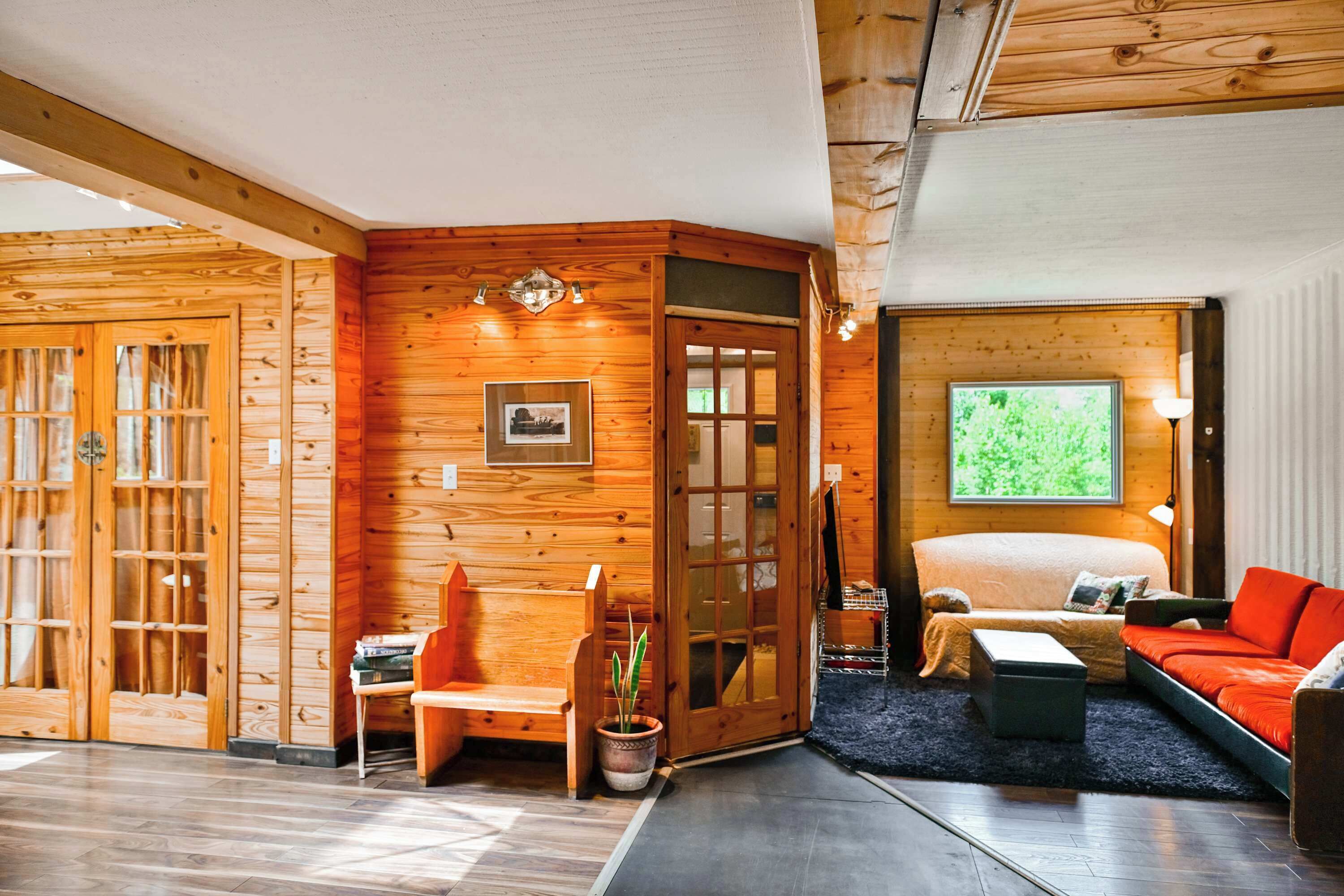 A cozy room with a bed, a red sofa, a wooden wall, and a window with a view.