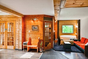 A cozy room with a bed, a red sofa, a wooden wall, and a window with a view. - Maison Conteneur d'Expedition (Amos)