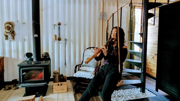 Interior rústico de una cabaña con estufa de leña, un columpio colgante y una zona de estar acogedora.