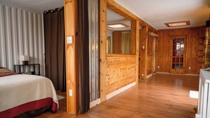 Una habitación de hotel con una cama, paredes de madera, suelo de madera y una puerta que conduce a otra habitación.
