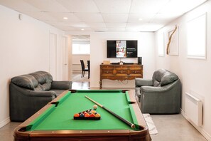 A room with a pool table, two leather sofas, a wooden cabinet, and a flat-screen TV mounted on the wall. - Lower Floor - Mont-Video (Barraute)